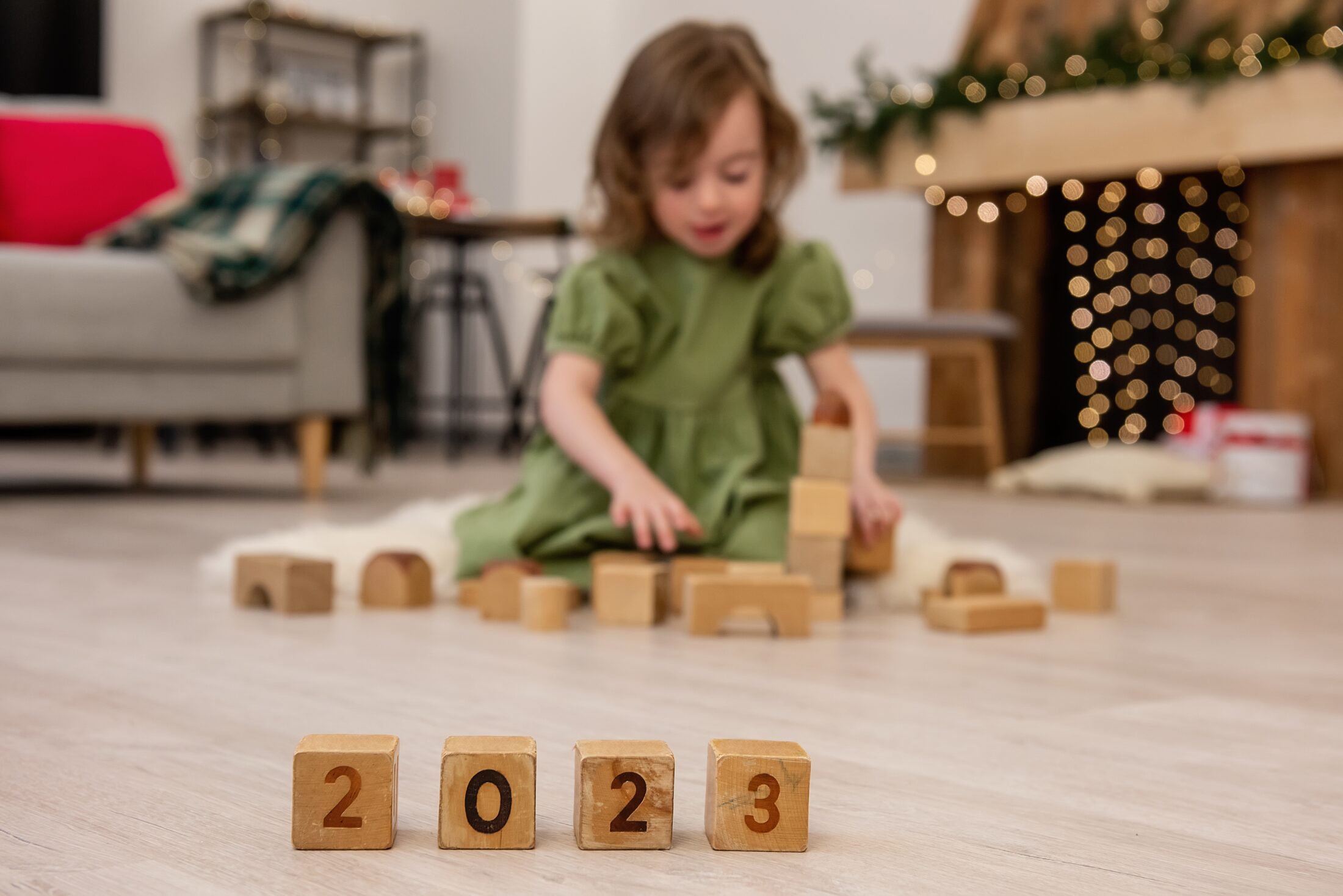 Wooden cubes with the numbers 2023 stand on the floor in a row. Background of a blurred happy girl